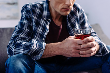 partial view of man with alcohol drink sitting on sofa at home