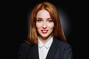 Portrait of a sexy red-haired girl on a black background. Beautiful business woman in a suit and shirt.