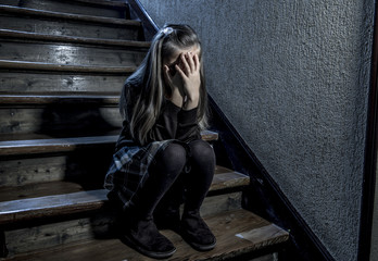 7 or 8 years old sad depressed and worried schoolgirl sitting on staircase desperate and scared suffering bullying and harassment at school