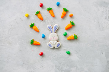 Easter bunny cookies and carrot chewing marmalade with candies on a white stone background. Top view and copy space.
