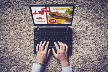 Top view of laptop with takeaway food service in the screen. Hands on the keyboard.