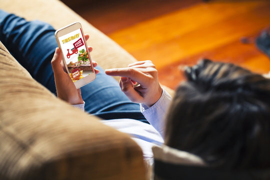 Woman ordering take away food by internet with a mobile phone while lying on a sofa.
