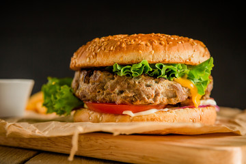 Burger with grilled beef, salad, cheese and tomato on dark background