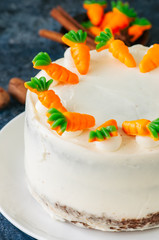 Carrot cake with cream cheese frosting decorated with carrot marmalade serving on a plate on a blue stone background.