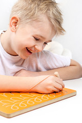 Edukacja dziecka w wieku przedszkolnym. Uśmiechnięty chłopiec ćwiczy pisanie literek. © Robert Przybysz