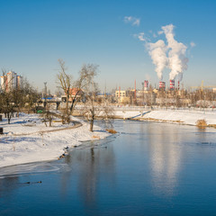 Fototapeta premium Thermal power plant during winter operation on the river bank. High chimneys emit a large amount of smoke