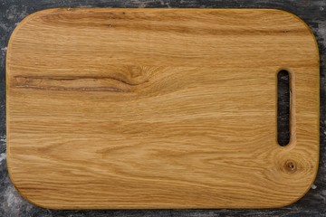 New wooden oak cutting board, rustic black background.