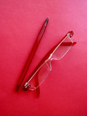 Red reading eyeglasses and red pen on red paper background