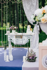 Decorative white vintage table at the wedding ceremony, candle-decorated books with flowers and ceramic angles and a cage on the purple carpet