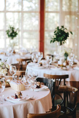 Decorated wedding table in rustic style for dinner with white and beige tablecloths, wine glasses for flowers and Viennese wooden chairs