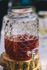 Morse or berry juice in glass jar beverage dispenser stands on a wooden slice