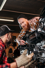 Fototapeta na wymiar handsome mechanics talking while repairing motorcycle together at garage