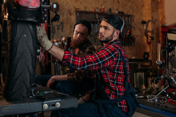 Obraz na płótnie Canvas handsome mechanics repairing motorcycle together at garage