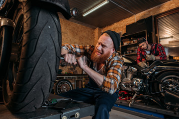 tensed mechanic fixing motorcycle while his colleague working on background