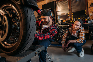 Fototapeta na wymiar tensed mechanic fixing motorcycle while his colleague sitting behind him at garage