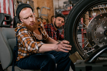 Fototapeta na wymiar handsome mechanics examining wheel of motorcycle at garage