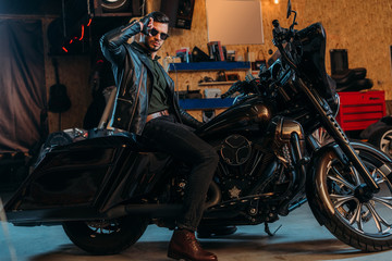 Fototapeta na wymiar handsome young man in sunglasses sitting on bike at garage