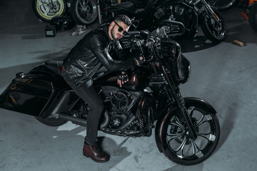 Plakat high angle view of handsome young man in sunglasses and leather jacket on bike at garage