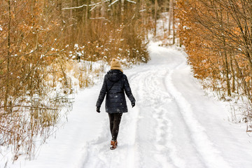 Naklejka premium Woman walking in snow at winter. Girl on snowy road in the forest.