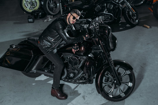 high angle view of handsome young man in sunglasses and leather jacket on bike at garage