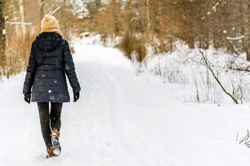 Woman walking in snow in winter clothes. Girl on snowy road in park.