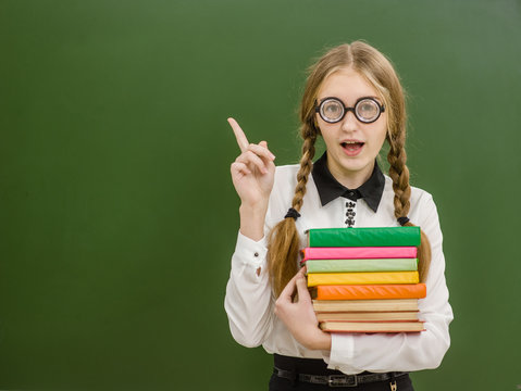 Smiling nerd student girl  with books on the background of a school board pointing away. Space for text