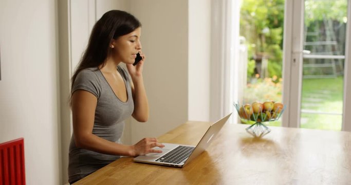 4K Attractive woman working from home, talking on phone & working on laptop. Slow motion.
