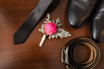 Groom’s accessories: flower boutonniere in focus, leather belt, necktie, shoes. Wedding
