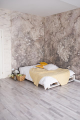 A loft style bedroom with recycled pallet bed. White and yellow bedding on bed with bedhead in loft bedroom interior