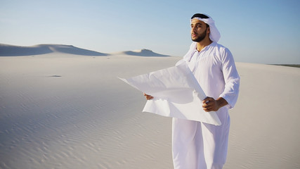 Handsome young Arabian UAE Sheikh male Arab businessman looks at future construction project plan...