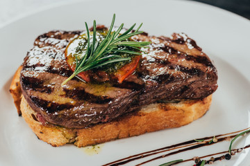 close-up view of delicious juicy beef steak with rosemary and roasted bread on plate