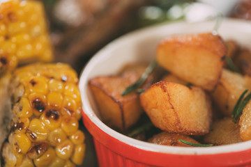 close-up view of tasty grilled corn with roasted potatoes on plate