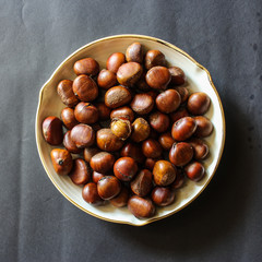 Fresh chestnuts on dark black rustic background. Pile of fresh chestnuts ready to roast shot over black antique background. Top view.