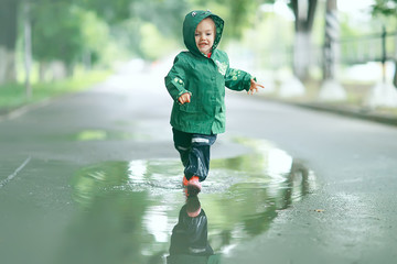 cheerful little girl walks and jumps in puddles in the rain