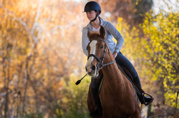 Obraz premium Young pretty girl - riding a horse with backlit leaves behind
