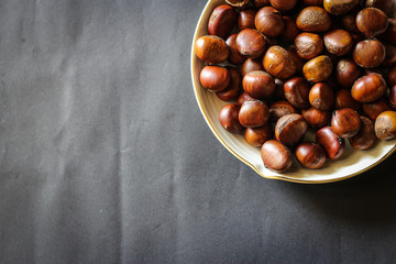 Fresh chestnuts on dark black rustic background. Pile of fresh chestnuts ready to roast shot over black antique background. Top view.
