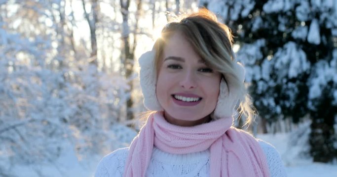 Portrait of beautiful happy girl with ear muffs, in frosty winter park. Outdoors. Flying snowflakes, sunny day. backlit. Smiling to camera, joyful cheerful mood,emotions