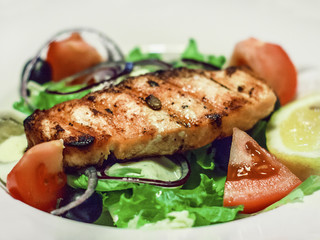 Salad with salmon, tomatoes and quail egg on a white plate