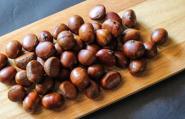 Fresh chestnuts on dark black rustic background. Pile of fresh chestnuts ready to roast shot over black antique background. Top view.