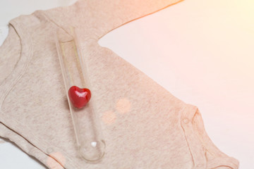 Baby clothes with vial and heart. Concept - IVF, in vitro fertilization. Waiting for baby, pregnant. Toned - 195141632