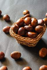 Fresh chestnuts on dark black rustic background. Pile of fresh chestnuts ready to roast shot over black antique background. Top view.