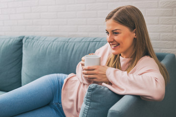 Beautiful woman enjoys drinking coffee while resting on sofa at her home.