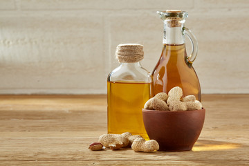 Fototapeta na wymiar Aromatic oil in a glass jar and bottle with peanuts in bowl on wooden table, close-up.