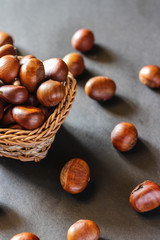 Fresh chestnuts on dark black rustic background. Pile of fresh chestnuts ready to roast shot over black antique background. Top view.