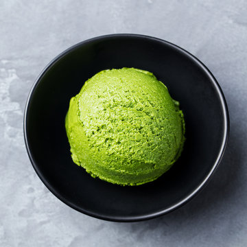 Green tea matcha ice cream scoop in black bowl on a grey stone background. Top view. Close up.