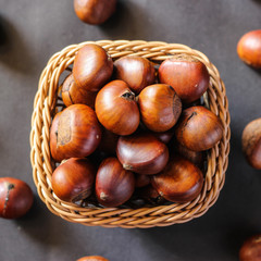 Fresh chestnuts on dark black rustic background. Pile of fresh chestnuts ready to roast shot over black antique background. Top view.