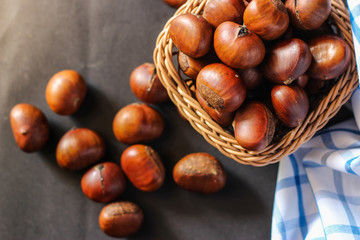 Obraz premium Fresh chestnuts on dark black rustic background. Pile of fresh chestnuts ready to roast shot over black antique background. Top view.