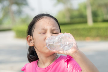 Happy Asian girl drinking a bottle of water outdoor.