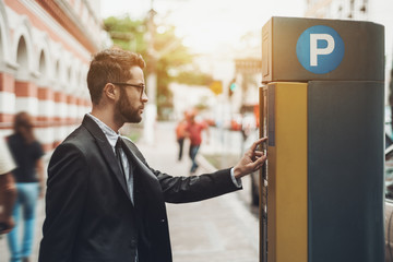 Young handsome businessman in glasses and the black business suit is paying his parking time using...