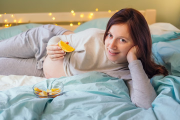Obraz na płótnie Canvas Sweet pregnant caucasian woman lying on bed with orange